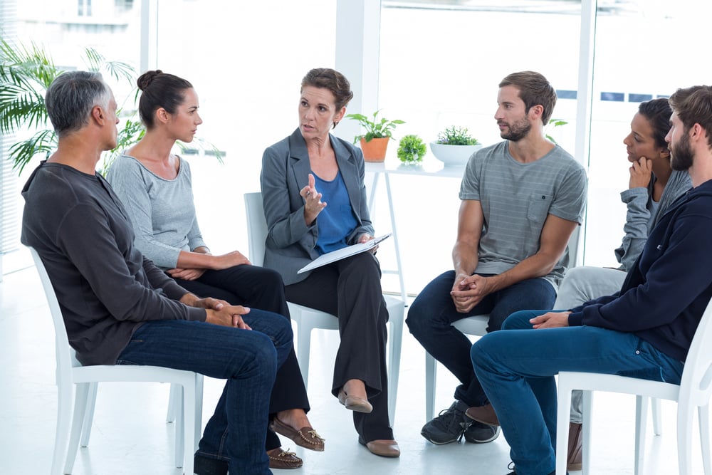 Group therapy in session sitting in a circle in a bright room Group therapy in session sitting in a circle in a bright room